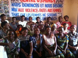 The women of Mamafrica, in front of a sign that reads "We Denounce and We Say NO to Violence Against Women!"